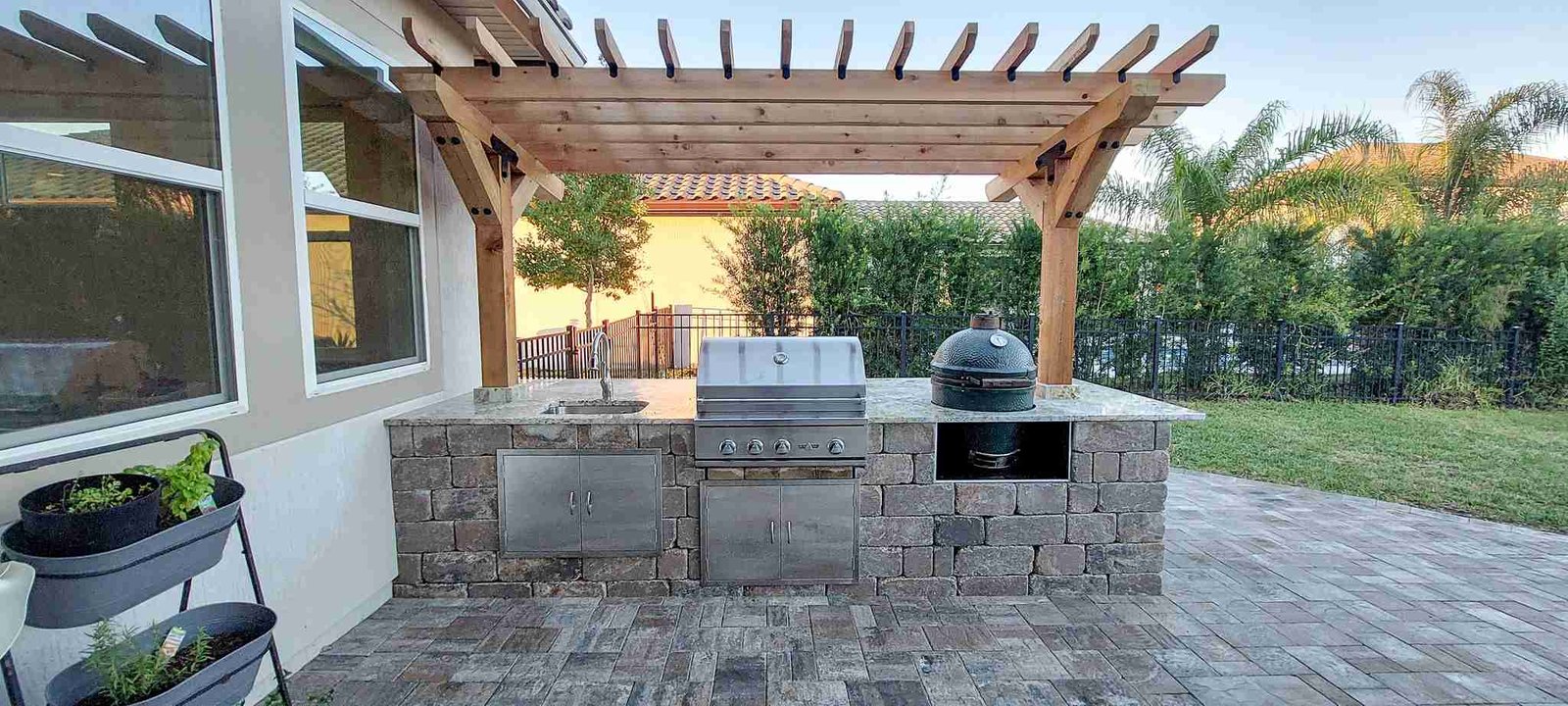 Wide-angle view of outdoor kitchen and pergola on paver patio