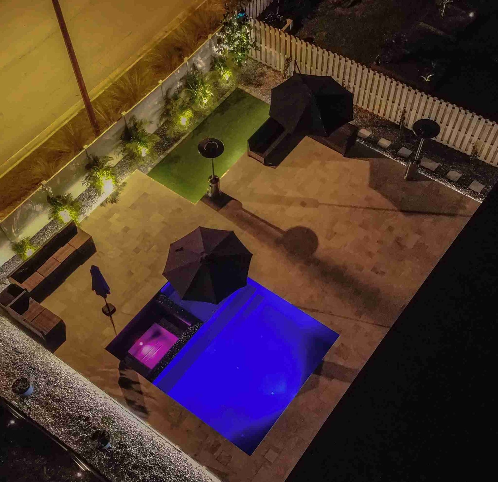 Aerial night view of backyard with lit pool, turf, and patio